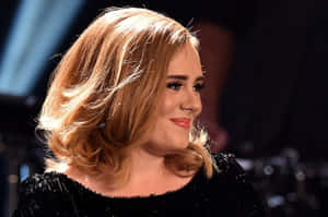 Adele 穿著黑色閃片上衣在舞台上微笑，金色頭髮。