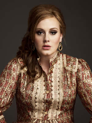 Adele 穿著金色和紅色圖案上衣，深色妝容和金色耳環。