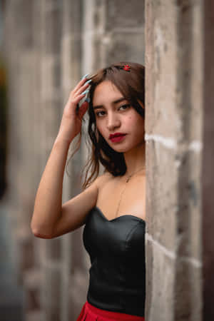 年輕女子從石牆後探出頭來，身穿黑色上衣和紅色裙子。