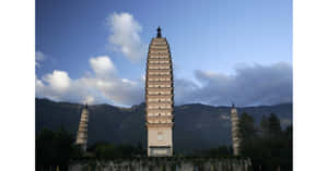 三座歷史悠久的石塔在藍天白雲下，高聳於山脈前。 — 建築 壁紙