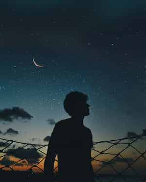 一個人透過圍欄在夜晚觀看彎月和星星的剪影。 — 夜晚 GIF 壁紙