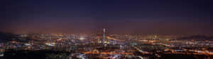 夜晚廣闊的城市，閃爍的燈光和突出的高塔。 — 32:9 壁紙