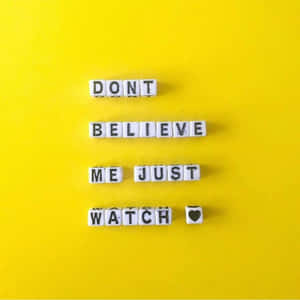 白色字母瓷磚在黃色背景上拼出「DON'T BELIEVE ME JUST WATCH ❤️」。