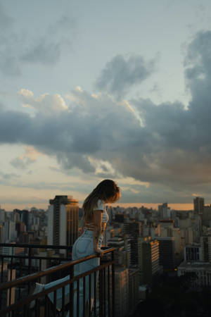 白衣女性從陽台俯瞰夕陽下的城市