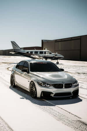 銀色BMW跑車停泊在積雪的機場，旁邊是一架小型飛機。