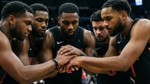五名身穿黑色球衣的籃球運動員在比賽中疊手圍圈。