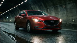 紅色Mazda房車在潮濕隧道中行駛，車頭燈亮起