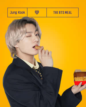 Jung Kook在黃色背景下從餐盒中吃雞肉。