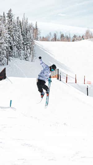 滑雪板運動員在半空中於雪坡上表演技巧，背景有松樹