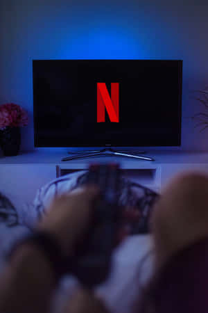 人在電視前拿著遙控器，電視在昏暗的藍光中顯示Netflix標誌。