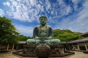 藍天白雲下寺廟庭院中的大型青銅佛像。