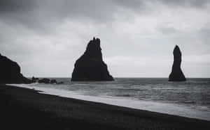 黑色的海蝕柱在黑色沙灘上，映襯著暴風雨的天空，高高聳立。 — 海灘 壁紙