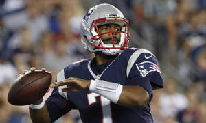 穿著愛國者隊制服的NFL四分衛在夜間體育場投擲橄欖球。