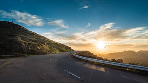 一個人在日落時分在彎曲的道路上奔跑，背景是山丘和天空。 — 美學 壁紙