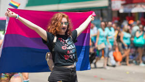 紅髮女子在LGBTQ遊行中手持雙性戀驕傲旗幟。