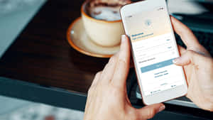 一個人喺咖啡杯旁邊登入應用程式。 — 16:9 壁紙