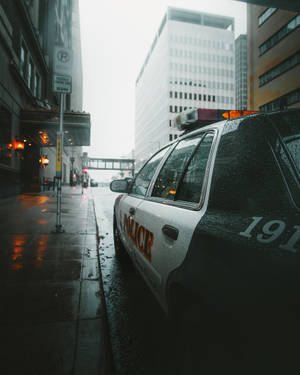警車停泊在黃昏時分濕漉漉的城市街道上，車窗上有雨滴。