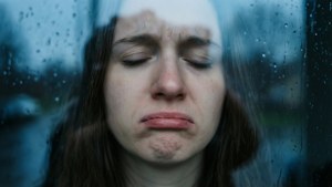透過雨窗看到一名閉著眼睛的悲傷女子。