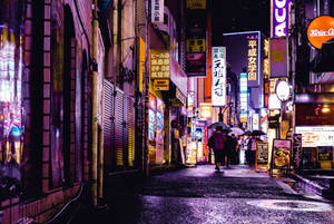 行人撐傘走過東京夜晚霓虹燈照亮的下雨小巷。