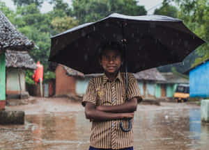 一個小男孩在黑色雨傘下微笑，在淹水且下雨的村莊街道上。 — 雨 壁紙