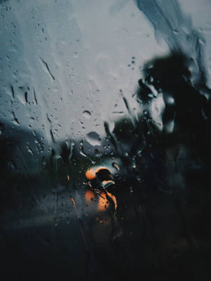 透過濺滿雨水的窗戶看到一個人的剪影，背後有橙色的光。