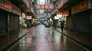 一個人在夜晚走過一條雨濕、霓虹燈照亮、商店關門的城市小巷。
