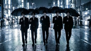 五個穿西裝的男人在夜晚的城市街道上撐傘雨中行走。 — Exo 壁紙