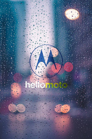 透過被雨水浸濕的窗戶可見 Motorola 標誌，背景是模糊的城市燈光。 — Motorola 壁紙