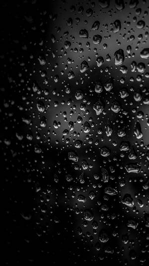 深色玻璃表面上雨滴的特寫，帶有柔和的光線反射。
