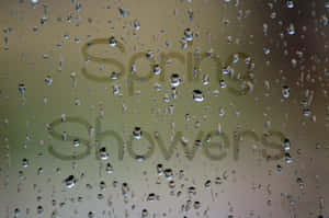 玻璃上的雨滴，背後有柔焦的「Spring Showers」文字。 — 3:2 壁紙