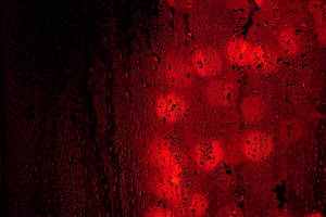 玻璃上的雨滴與黑暗中模糊的紅光。 — 雨 壁紙