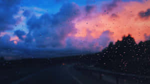 車窗上的雨滴，黃昏時分蜿蜒的道路和色彩繽紛的雲彩 — Studio Display 壁紙