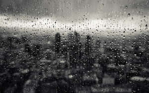 玻璃上的雨滴遮蓋了模糊的城市天際線，呈現灰階色調。 — 雨天 壁紙