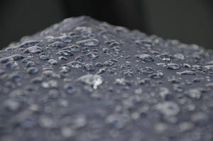 在柔焦中，深色紋理表面上的閃爍雨滴。