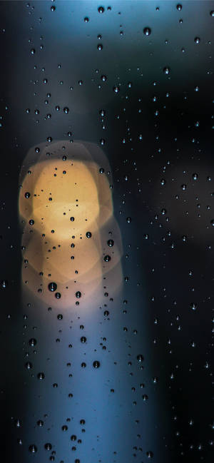 窗戶上的雨滴，背景有模糊的暖光。 — 深色iPhone壁紙