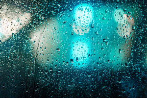 窗戶上的雨滴，夜晚模糊的藍綠色城市燈光。