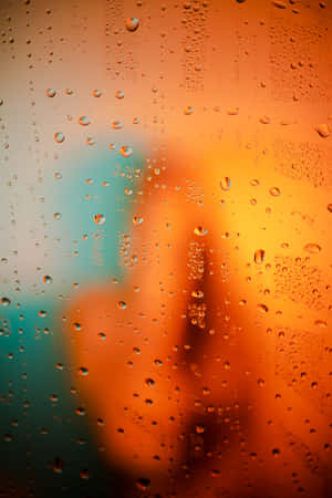 黃昏時窗戶上的雨滴，模糊的橙色和藍綠色城市燈光。