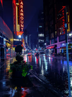 雨夜城市街道，霓虹燈光在濕漉漉的人行道上反射，並有Paramount劇院標誌。 — iPad 第9代 壁紙