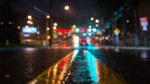 雨夜街道，模糊的燈光反射在潮濕的人行道和黃線上。 — 4K桌面壁紙