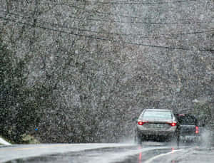 銀色汽車在暴風雪中行駛在濕滑道路上，有光禿禿的樹木