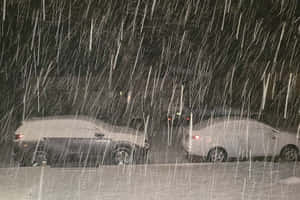 夜間暴風雪中，兩輛停在外面的積雪汽車。 — 夜晚 GIF 壁紙