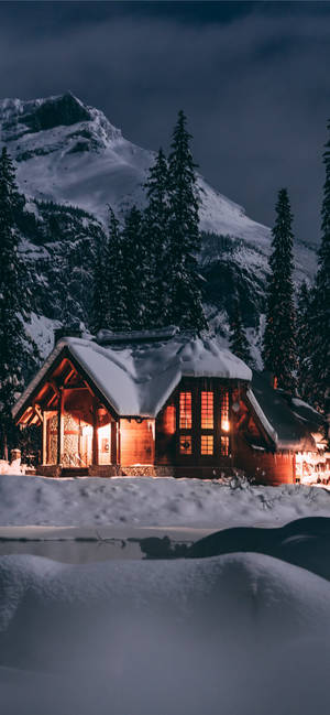 舒適小屋在夜間雪中發光，背景有山脈