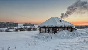 冬日景色中，夕陽下雪覆蓋的木屋冒著煙。