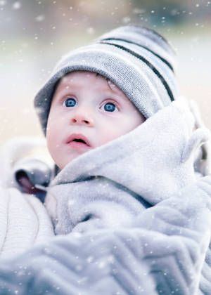 一個穿著冬季裝備的嬰兒，在雪花輕輕飄落時向上看。