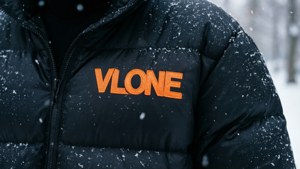 黑色羽絨外套，帶有橙色Vlone標誌，覆蓋著雪花