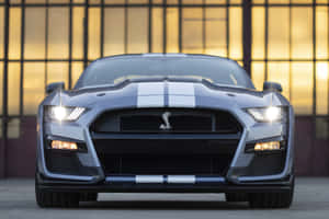 銀色Shelby GT500跑車，帶有白色條紋，停在夕陽映照的工業建築前。