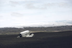 廢棄的飛機機身置於黑色火山土壤上，背後有雪山。