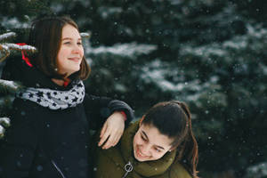 兩位女性在雪地森林中微笑擁抱。