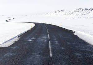 一條蜿蜒的道路穿過白雪皚皚的冬季景觀，遠處有山脈。 — 山景 壁紙