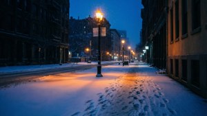 夜晚被雪覆蓋的城市街道，溫暖的路燈照亮，雪地上有腳印。